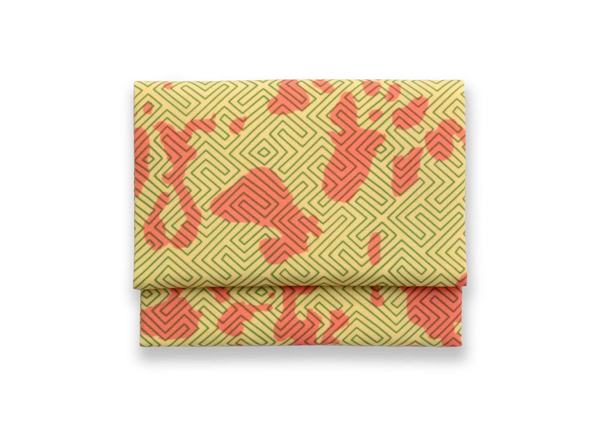 Bright patterned cloth napkin with quarter-inch hem. Base color is mustard yellow with random splotches of brick red, overlaid with a thin-lined, maze-like pattern in rosemary green. The back is the base color with small, discreet dark grey logo on bottom left-hand side. View: 1 napkin folded into a rectangular shape for a table setting, with pattern side exposed.